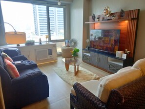 A living room with a sofa, a TV, a fan, and a decorative shelf. - Exquisite Condo Unit in Eastwood (Quezon City)