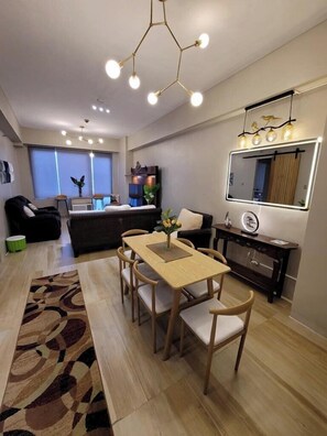 A modern living room with a dining area, a large mirror, and a ceiling light fixture. - Exquisite Condo Unit in Eastwood (Quezon City)