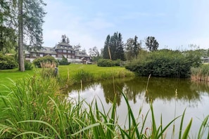 A large building with a symmetrical facade, a pond in the foreground, and a well-maintained lawn.