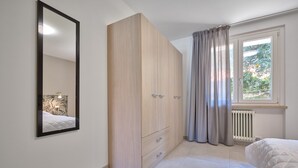 Ein Schlafzimmer mit großem Kleiderschrank, einem Bett, einem Fenster mit Vorhängen und einer Heizung.