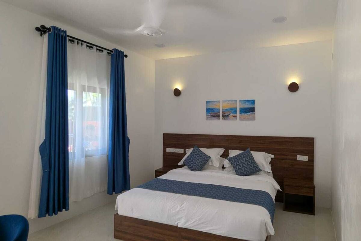 Un dormitorio con cama, cortinas, luces fijadas a la pared y un cuadro.