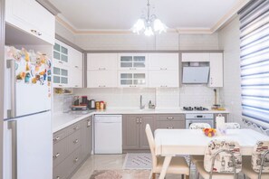 Une cuisine moderne avec des meubles blancs, un lave-vaisselle, une table à manger avec des chaises et un lustre.