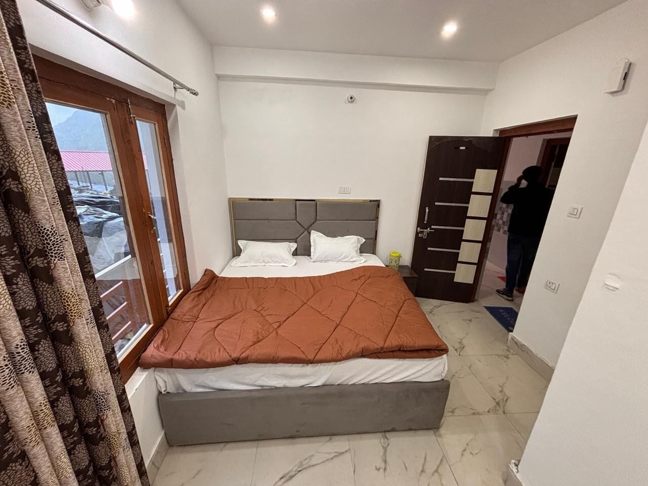 A bedroom with a bed, curtains, a window, and a door.