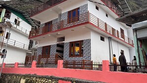 A two-story building with balconies, a stone wall, and a red fence. - Omji Temple View Kharsali (Rajgarhi)