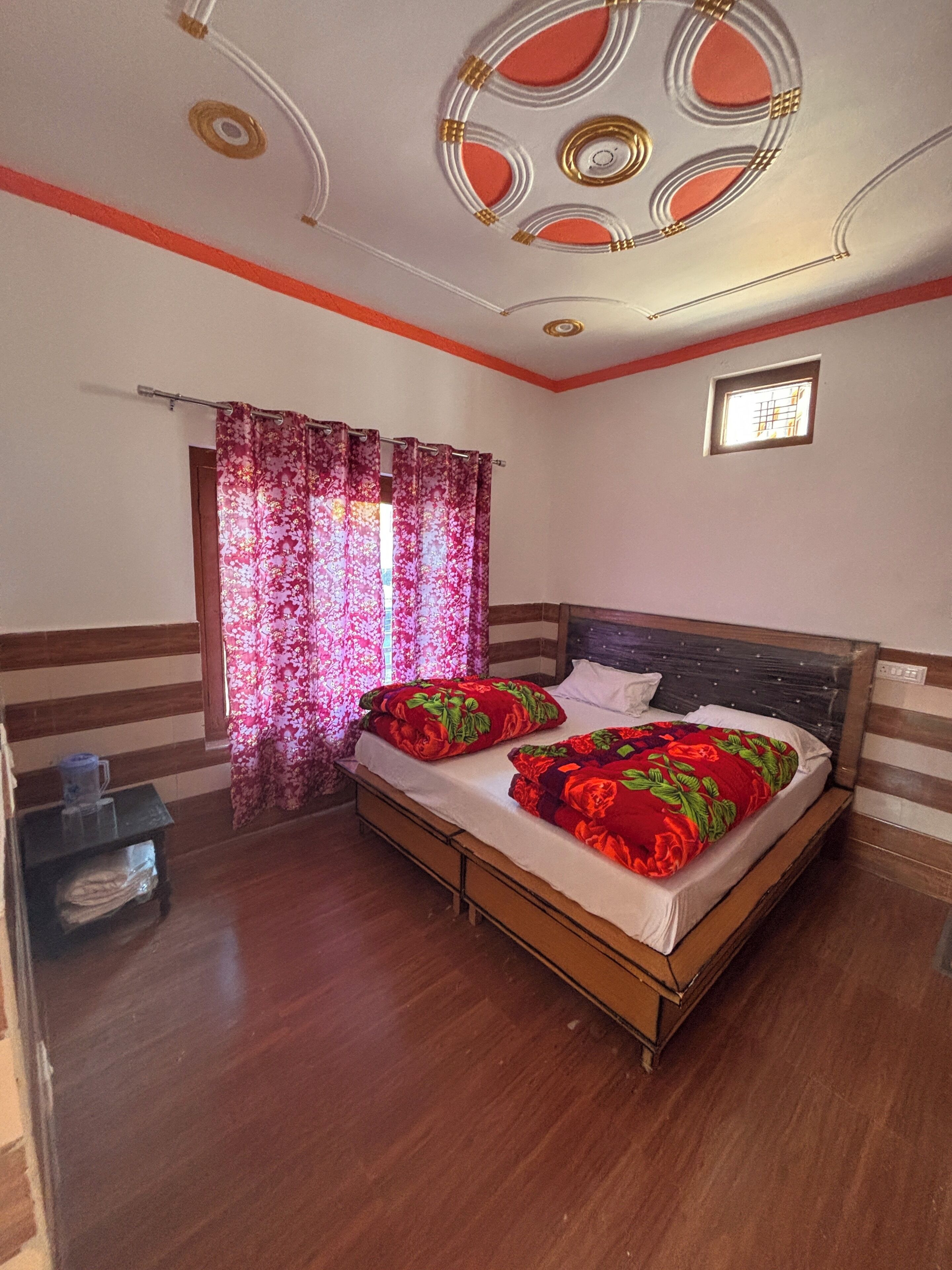 Un dormitorio con cama de madera, cortinas florales, un ventanal pequeño y techo con diseños decorativos.