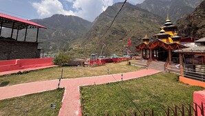 A mountainous landscape with a temple, a red-roofed building, and a paved walkway. - Omji Temple View Kharsali (Rajgarhi)
