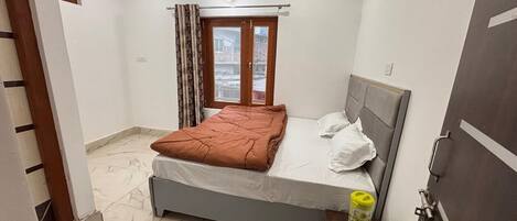 A bedroom with a bed, a window, and a door.
