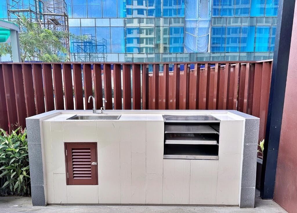 An outdoor kitchen with a sink and ventilation, set against a modern building with reflective glass windows.