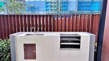 An outdoor kitchen with a sink and ventilation, set against a modern building with reflective glass windows.
