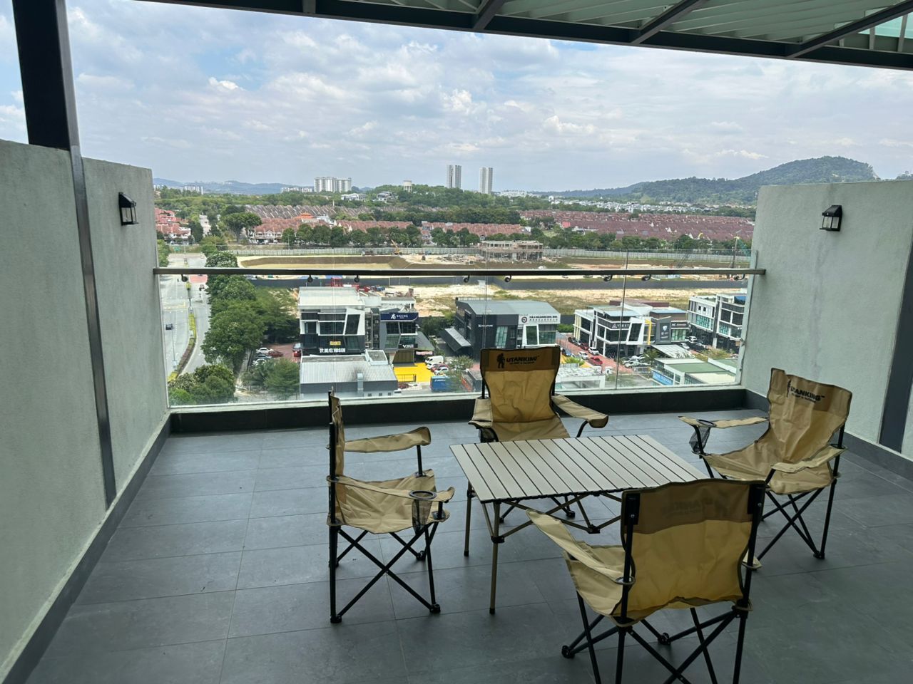 A balcony with a table and chairs, a view of a cityscape, and a clear sky.