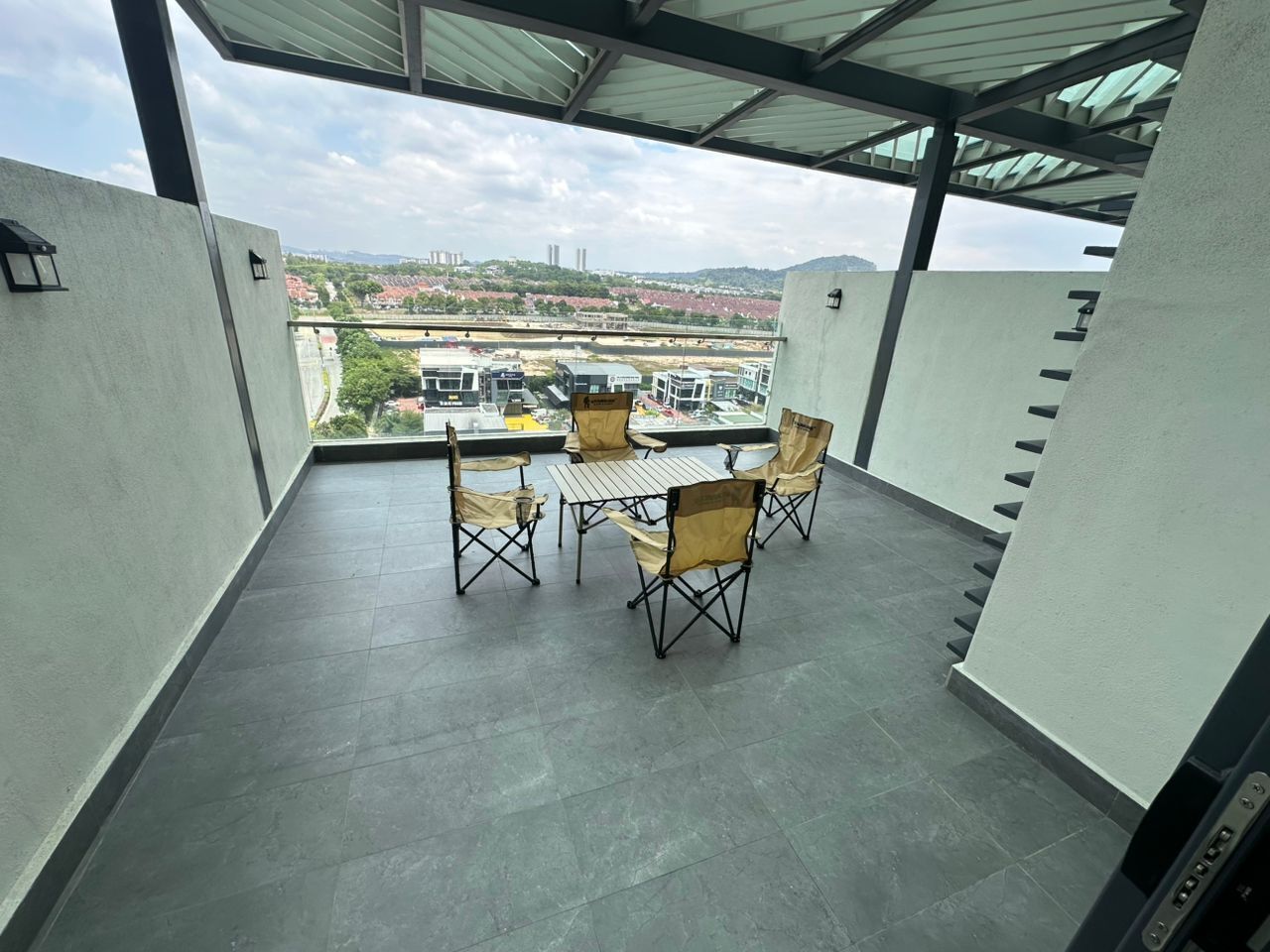 Ein Balkon mit Tisch und Stühlen, Blick auf Gebäude und Grünflächen, sowie ein überdachter Bereich mit Metallveranda.