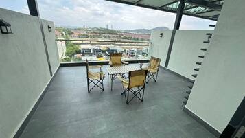 Ein Balkon mit Tisch und Stühlen, Blick auf Gebäude und Grünflächen, sowie ein überdachter Bereich mit Metallveranda.