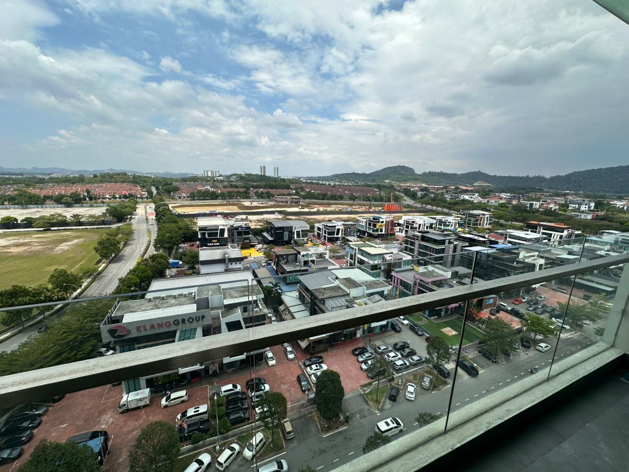 A commercial area with multiple buildings, a parking lot, and a distant view of a hilly landscape.