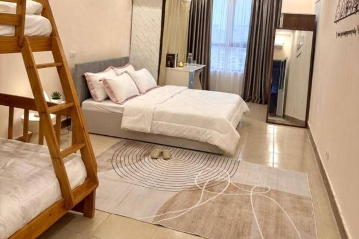 Une chambre d’hôtel avec un lit superposé, un lit simple, un miroir, un bureau et une vue sur l’extérieur.