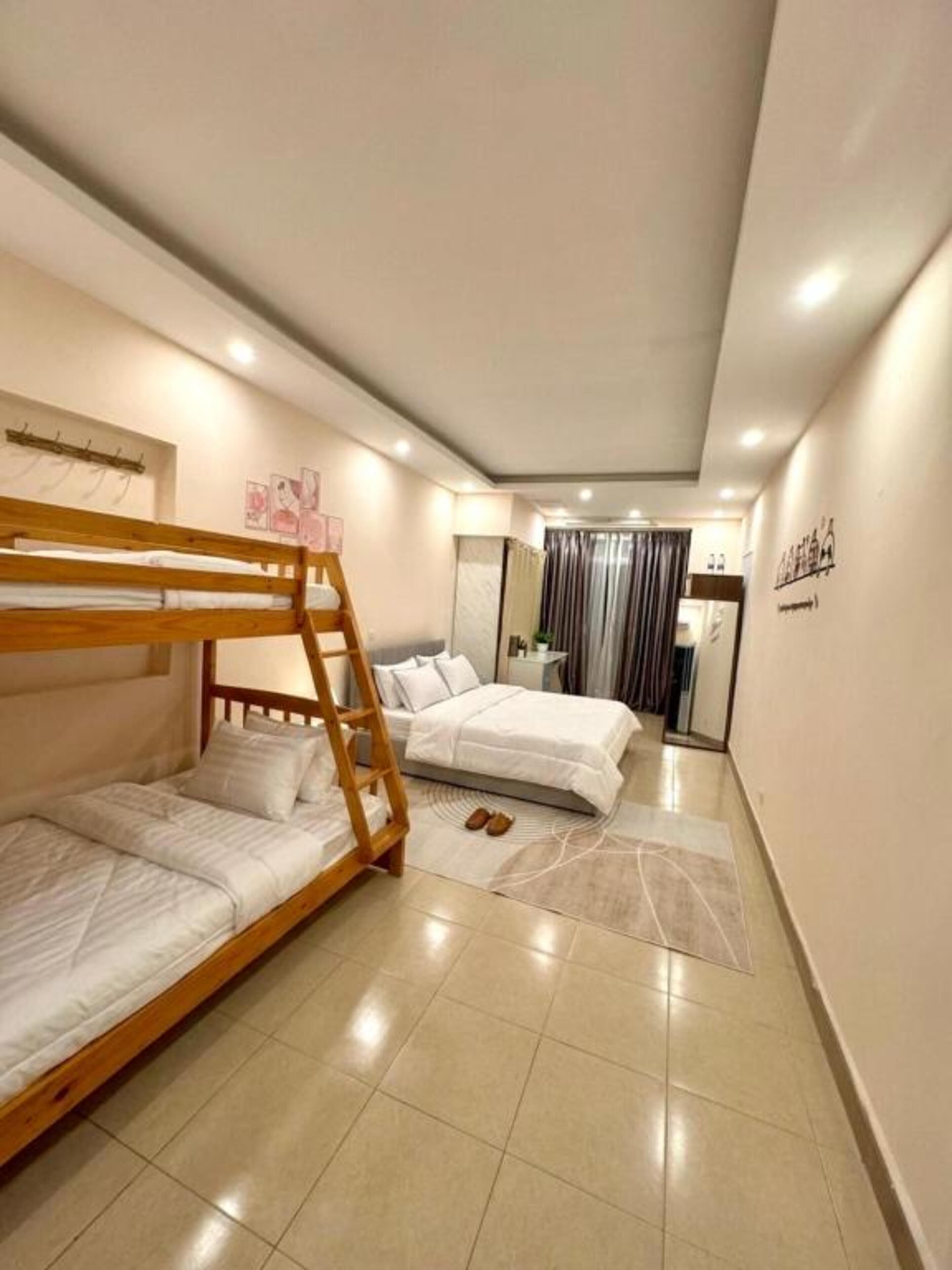 A bedroom with two beds, a wooden bunk bed, a bathroom with a mirror, and a tiled floor.