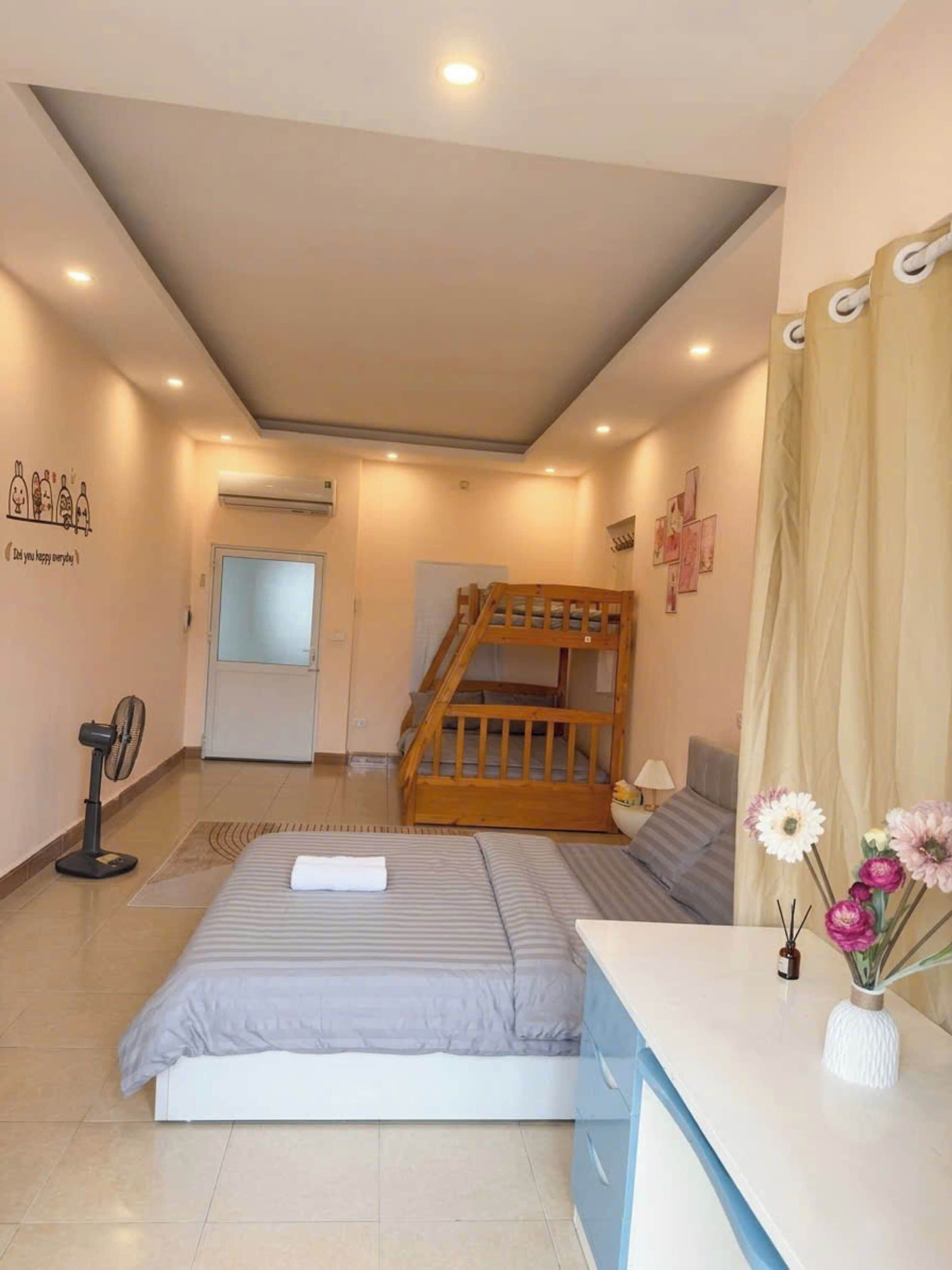 A bedroom with a bunk bed, a desk, a chair, a fan, a window, and a wall decoration.
