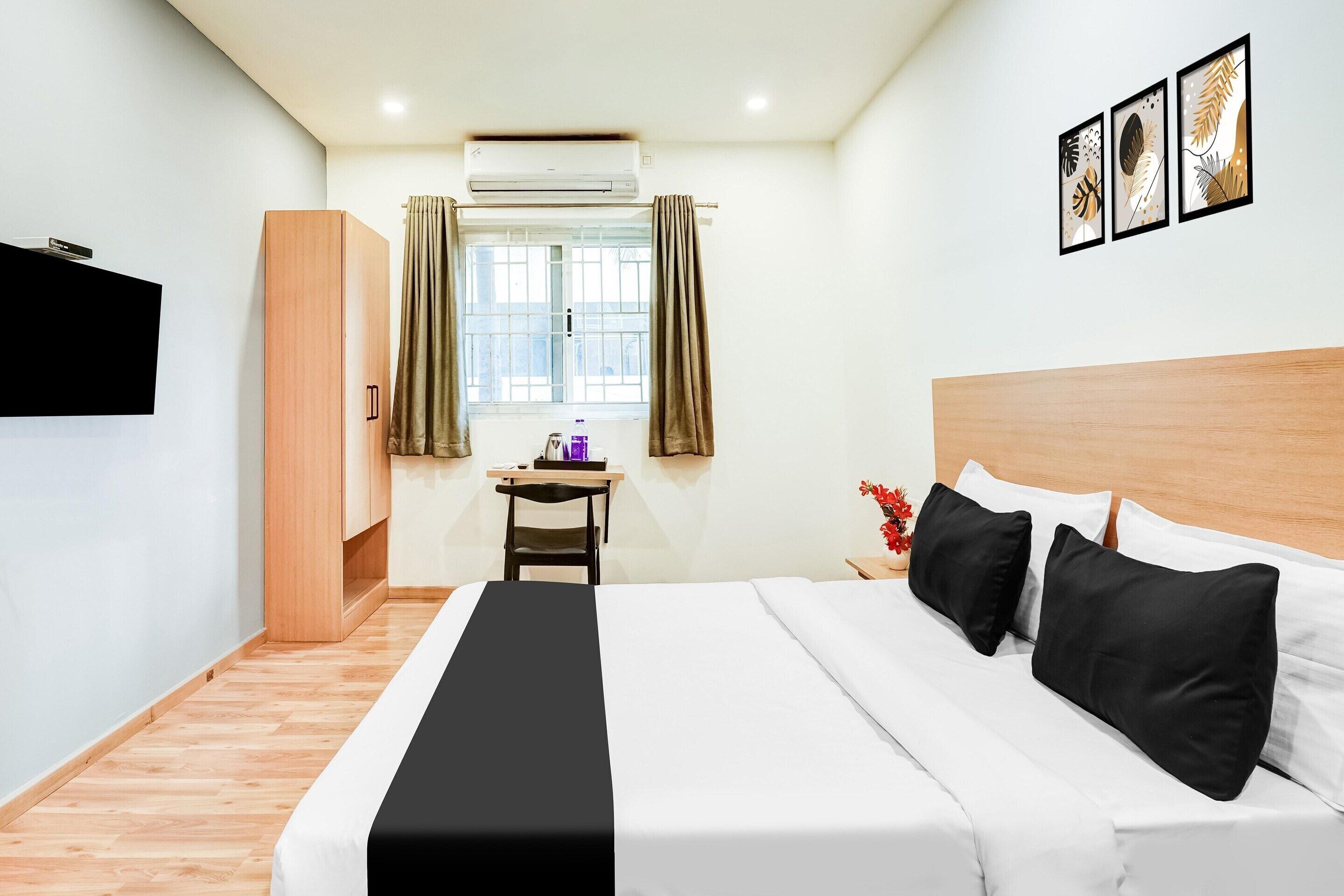 A hotel room with a bed, a desk, a chair, an air conditioner, a TV, and a window with curtains.