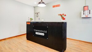 Ein Empfangsschalter mit der Aufschrift 'TOWNHOUSE', einem Schild 'Company-Serviced', einem 'WiFi Zone'-Schild, einer Überwachungskamera und einem kleinen Topfpflanzen.