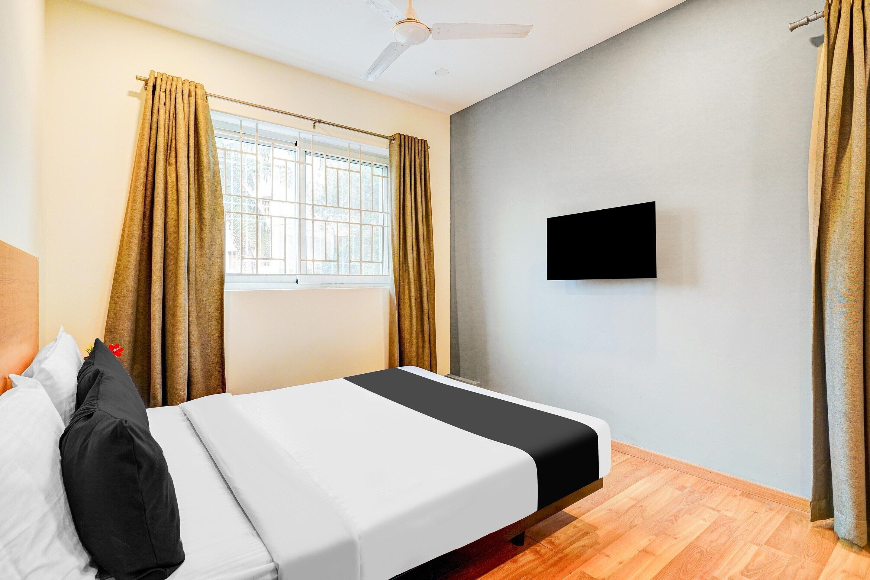 A hotel room with a bed, curtains, a ceiling fan, a window, and a flat-screen TV.