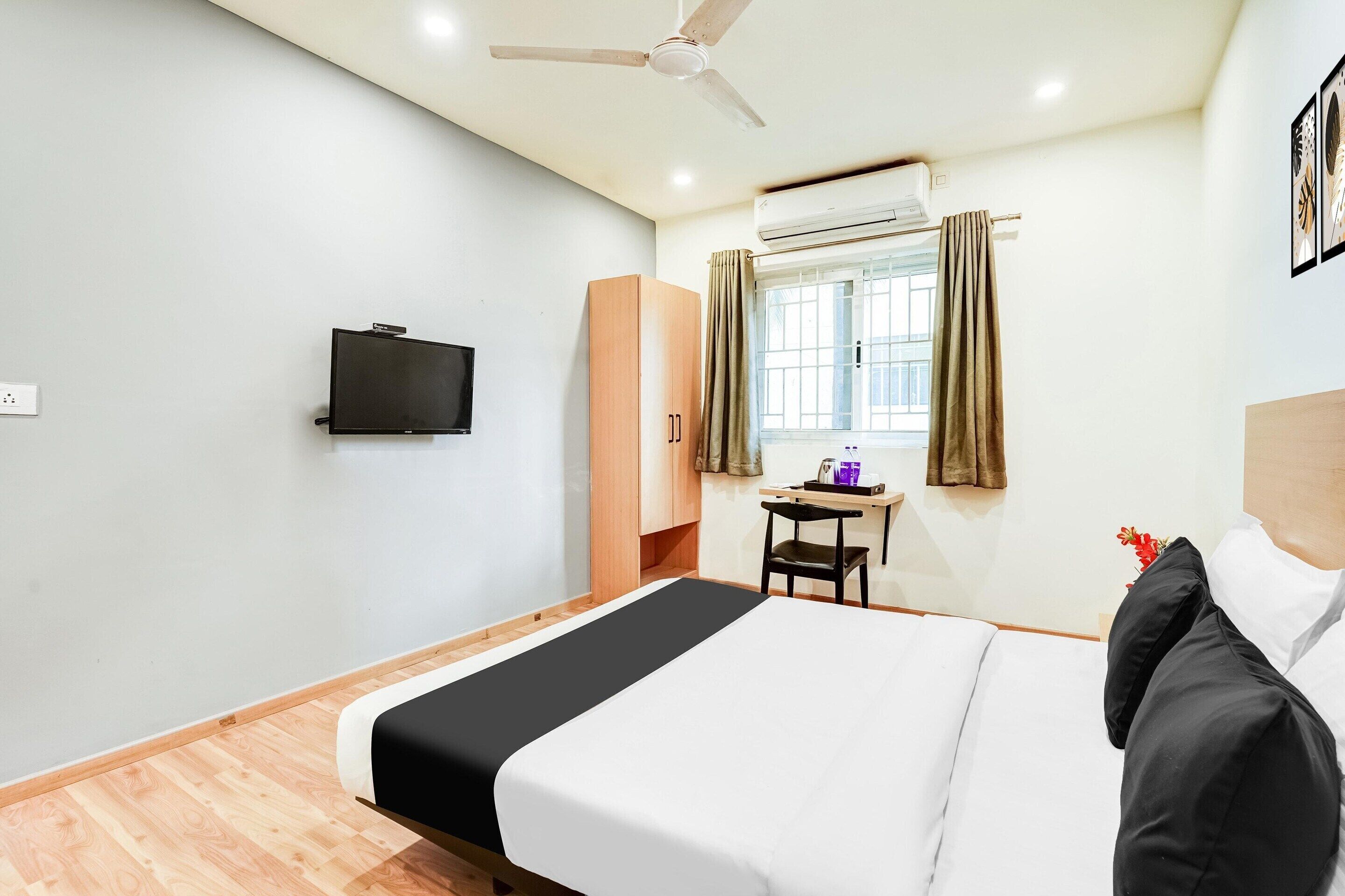 A hotel room with a bed, a desk, a chair, a television, an air conditioning unit, and a window with curtains.
