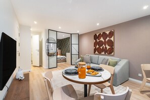 Ein modernes Wohnzimmer mit Essbereich, Fernseher und einer Küche im Hintergrund.