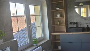A bathroom with a window, a towel rack, a sink, a mirror, and shelves with toiletries. - Dworek Dębówko Jadwiga Jeżewicz (Bartoszyce)