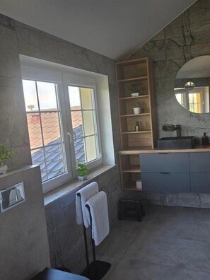 A bathroom with a window, a towel rack, a sink, a mirror, and shelves with toiletries.