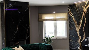 A modern living room with a green sofa, a white coffee table, a marble accent wall, and a window with a view. - Dworek Dębówko Jadwiga Jeżewicz (Bartoszyce)