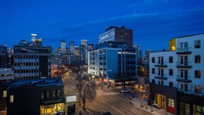 Un paisaje urbano al anochecer con edificios modernos, una clínica y una calle con coches y peatones.