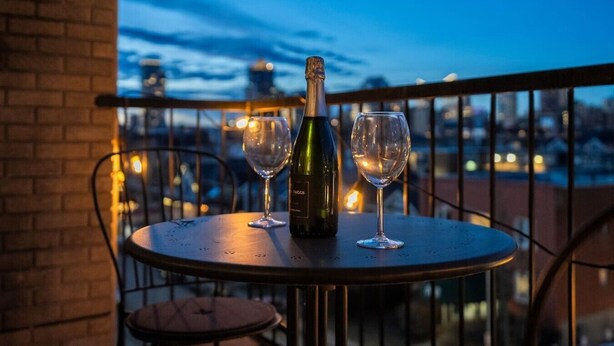 Una mesa con una botella y dos vasos en un balcón con vistas a la ciudad al anochecer.