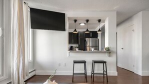 Una cocina moderna con televisor de pantalla plana, luces colgantes y refrigerador de acero inoxidable.