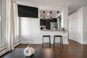A modern kitchen with a flat-screen TV, pendant lights, and a stainless steel refrigerator. - Mins to Saddledome | UG Parking | 2 Bed | Central (Calgary)
