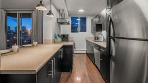 Una cocina moderna con electrodomésticos de acero inoxidable, piso de madera y vistas a la ciudad a través de amplios ventanales.