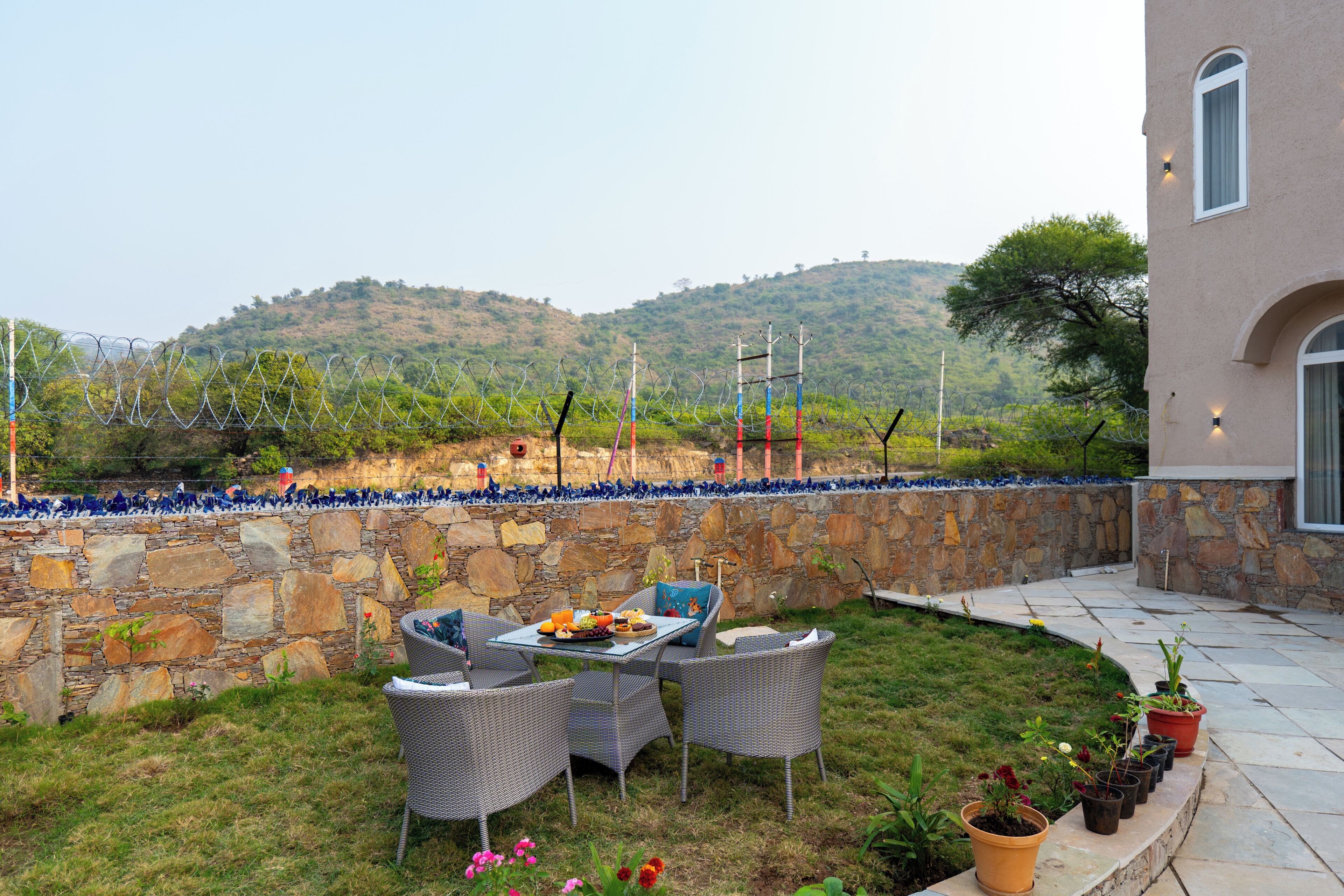 Un patio exterior con paredes de piedra, mobiliario de mimbre y plantas en macetas.