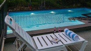 Une piscine entourée d’une rambarde en métal, avec des chaises longues et une table à proximité.