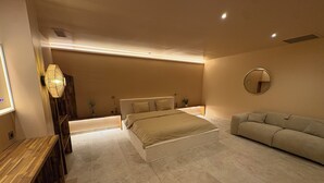 Une chambre à coucher moderne avec un lit, des tables de chevet, un canapé et un miroir.