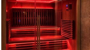 Un sauna avec des bancs en bois et une enceinte en verre, éclairé par un éclairage rouge.