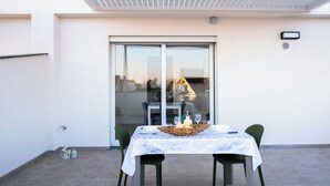 Un balcon avec une table dressée pour deux personnes, une chaise, une petite plante et une fenêtre donnant sur des immeubles.
