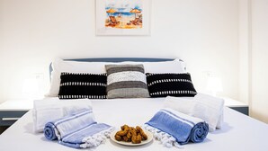 Un lit bien fait, agrémenté de serviettes, une assiette de collations et un tableau sur le thème de la plage accroché au mur.