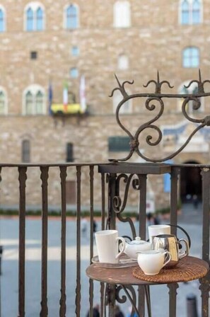 Un balcon avec une table où sont disposés des tasses et une théière, donnant sur un bâtiment doté de fenêtres en arc de cercle.