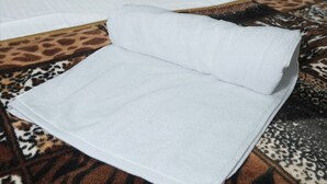 A bed with a white pillow and a folded white towel on a patterned rug. - Omji Ashram Varanasi (Varanasi)