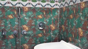 A bathroom with a white toilet, a shower with a handheld showerhead, and a patterned tile wall. - Omji Ashram Varanasi (Varanasi)