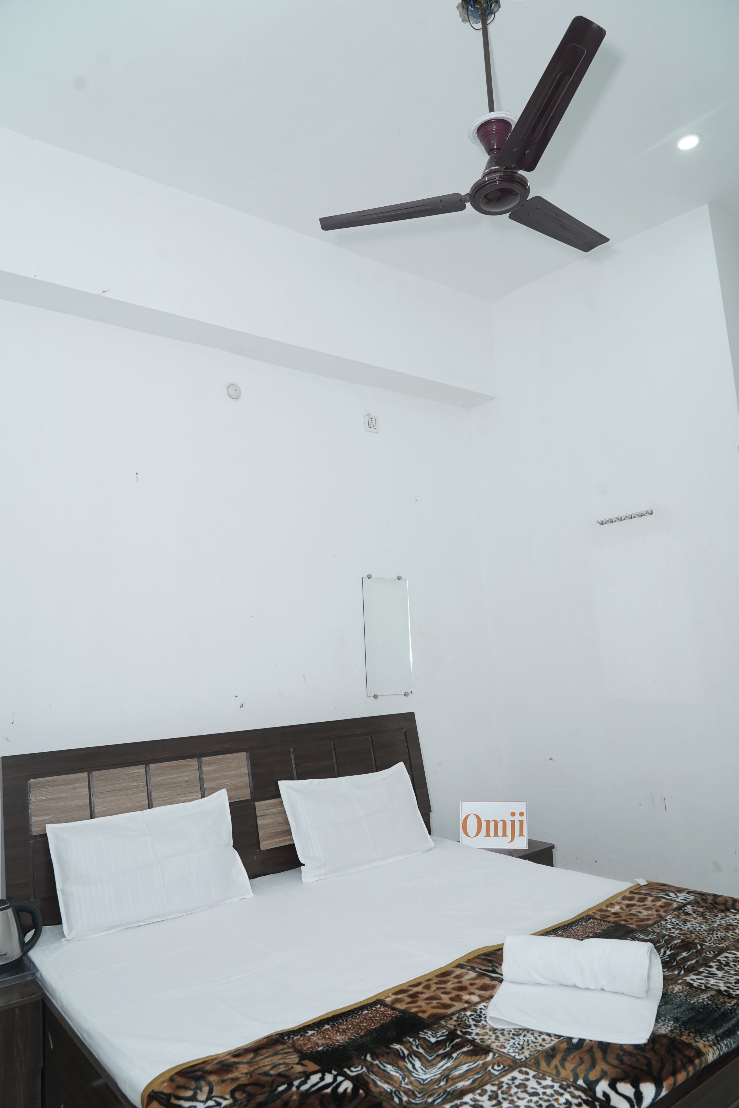 A hotel room with a bed, a ceiling fan, a nightstand, and a sign with 'Omji' on it.