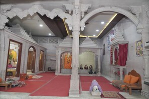 Interior ornamentado de un templo con una deidad central, suelo de moqueta roja y asientos tradicionales.