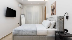 Un dormitorio moderno con cama, mesita de noche, televisión, aire acondicionado y una obra de arte en la pared.