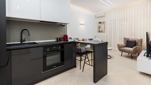 Una cocina moderna con encimera negra, electrodomésticos de acero inoxidable y una zona de comedor con mesa y sillas blancas.