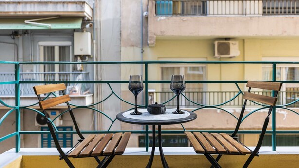 Un balcón con una mesa, dos sillas y dos copas de vino.