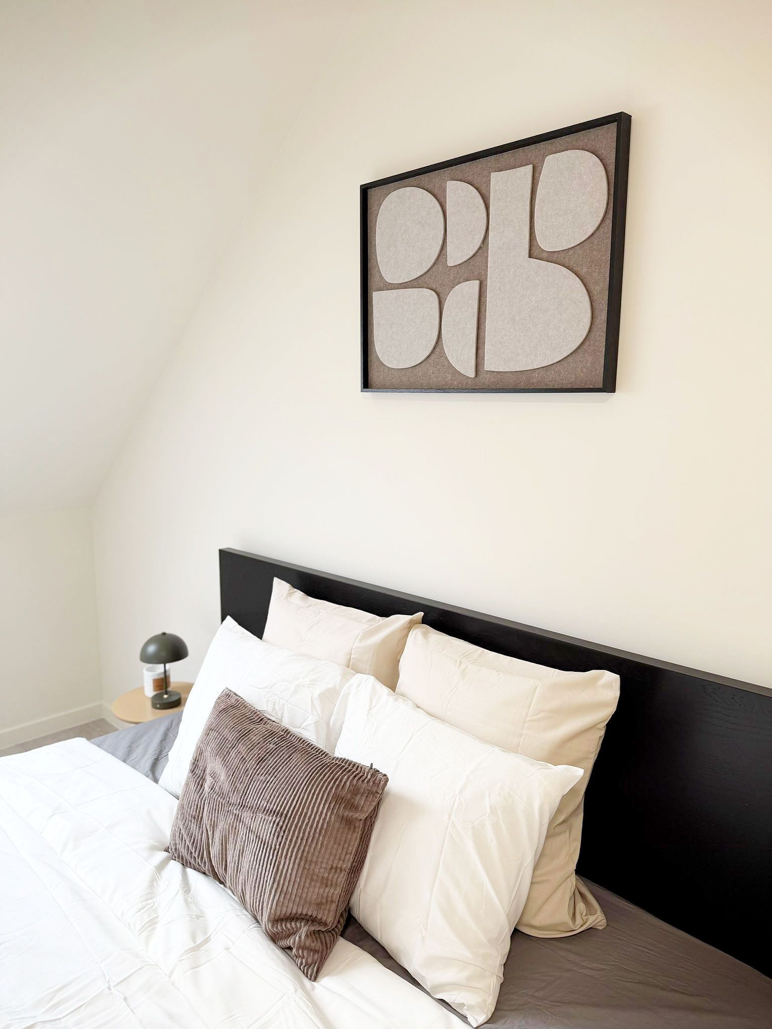 A neatly made bed with white and brown bedding, a black headboard, and a wall-mounted abstract art piece.
