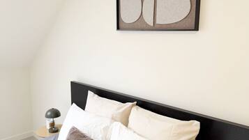 A neatly made bed with white and brown bedding, a black headboard, and a wall-mounted abstract art piece.
