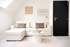 A modern living room with a sectional sofa, a round coffee table, a black door, and a white wall with a shelf. - Spacious Rooms 15 Min to City Center (Ghent)
